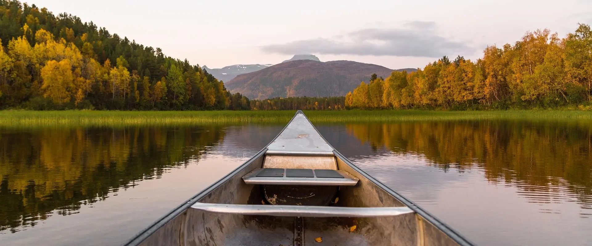 A canoe on a still Kentucky lake at dawn, framed by autumn forest and distant mountains